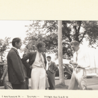 Group of men and women standing outside with trees and car in background.