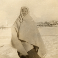 9-9-p: Woman, standing outside with blanket wrapped around head and shoulders.