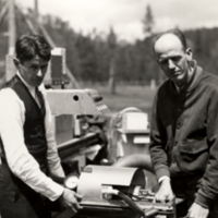 Two unidentified men, standing outside, working on equipment for stratospheric flight, 3/4 view.