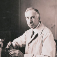 Rufus Cole, half length, informal, sitting at desk in laboratory holding dropper.