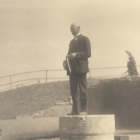 Man standing on platform, holding hat.