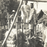 Four unidentified men, full length, standing with a native hemp press, Philippines.