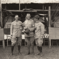 Three men standing outside in uniform, building in background.