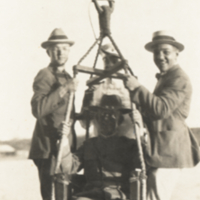 Four men, one seated in chair, three holding on to side, being lifted above water.