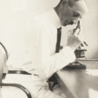 Leo Loeb, seated at table, looking into microscope.