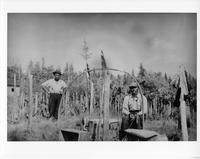 A-322: Two Ojibwa men, portrait, near ornamental poles 