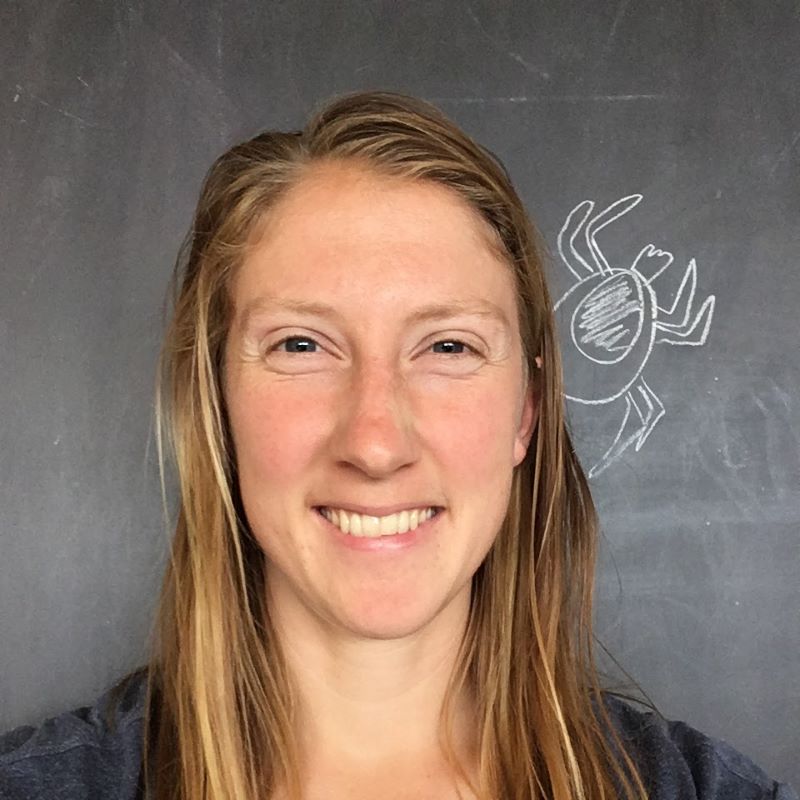 Headshot of Lisa Couper in front of a blackboard with a tick scribbled on it.