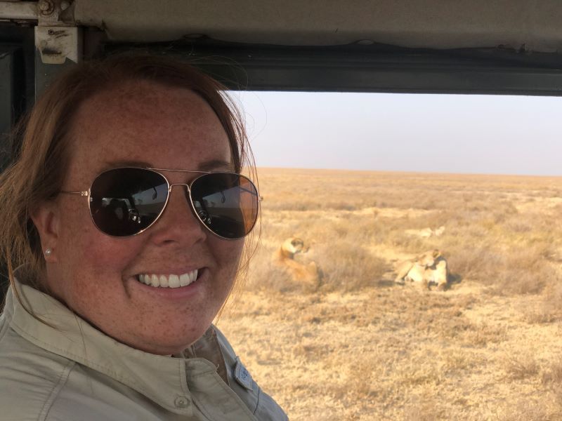 Katherine Fowler in a vehicle on the savannah with lions in the background