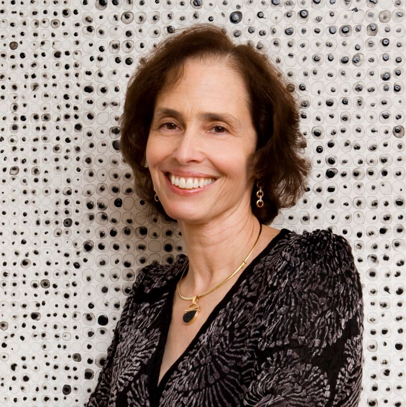 A woman with brown hair is standing in front of a wall filled with images of cells.