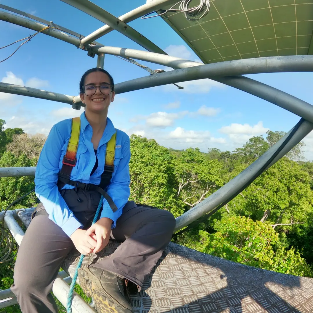 Juliana Rubinatto Serrano seated outside on a structure above tree canopy.